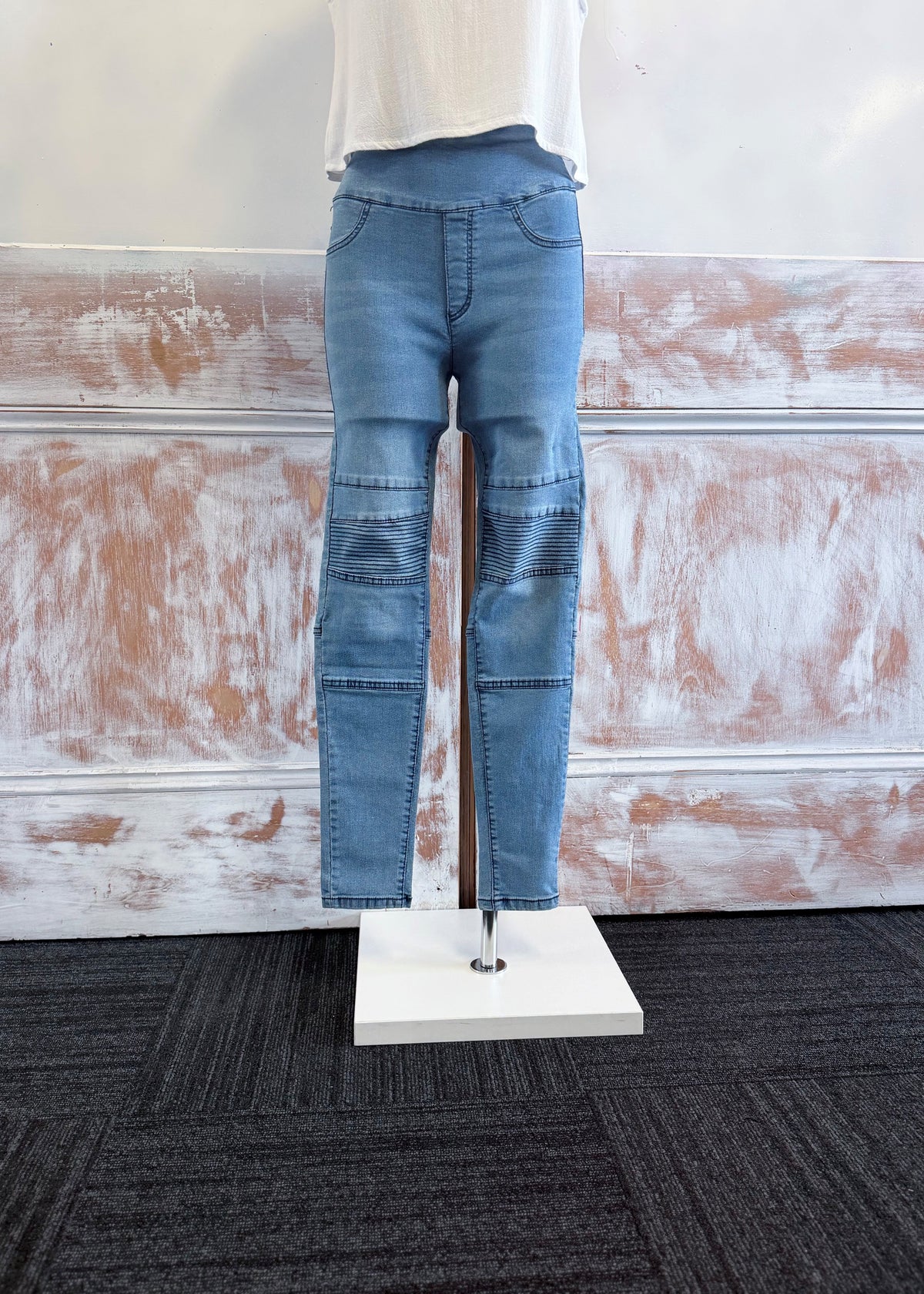 Blue jeans on a mannequin stand against a textured wall.
