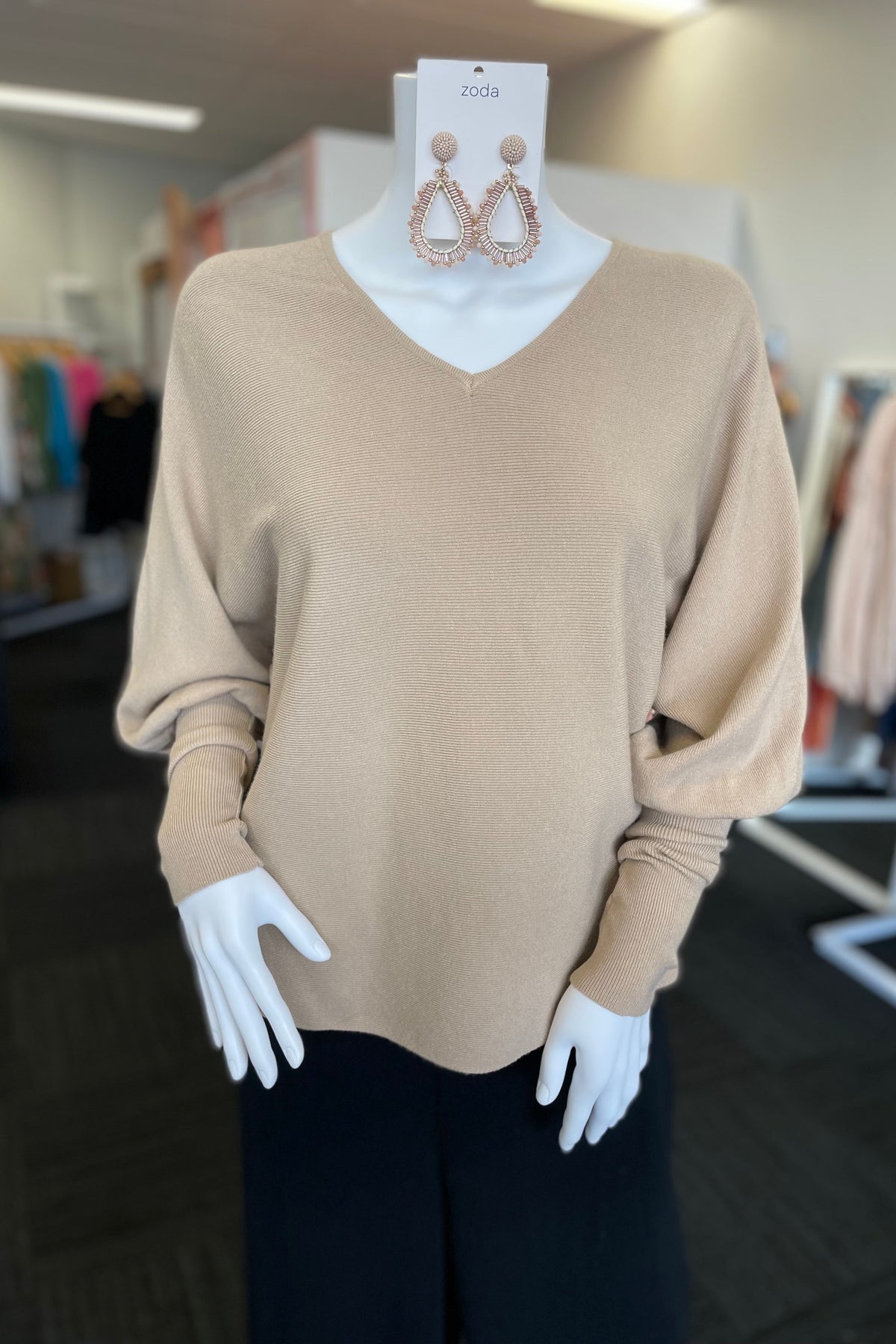 A mannequin wearing a beige v-neck box jumper with long sleeves.