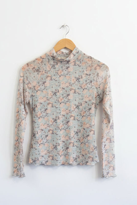 Floral long-sleeve top on a wooden hanger against a rustic wooden wall.